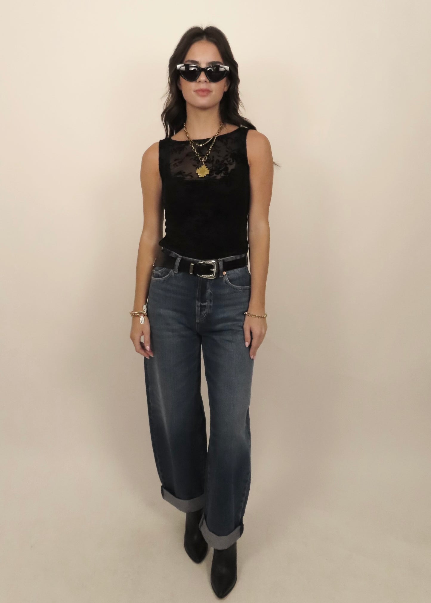 Woman wearing a black sleeveless top and jeans with sunglasses on a beige background