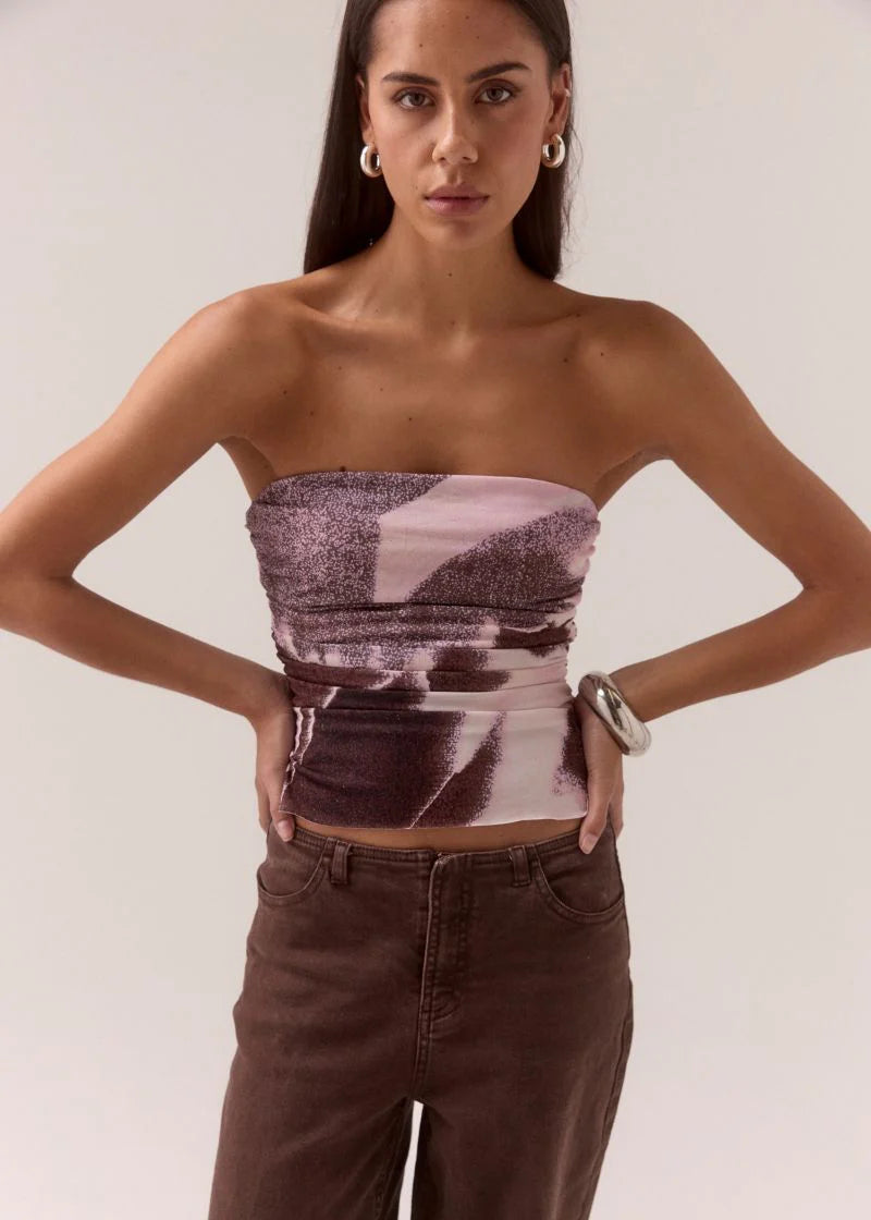 Woman wearing a strapless top with abstract pattern and high-waisted pants on a plain background