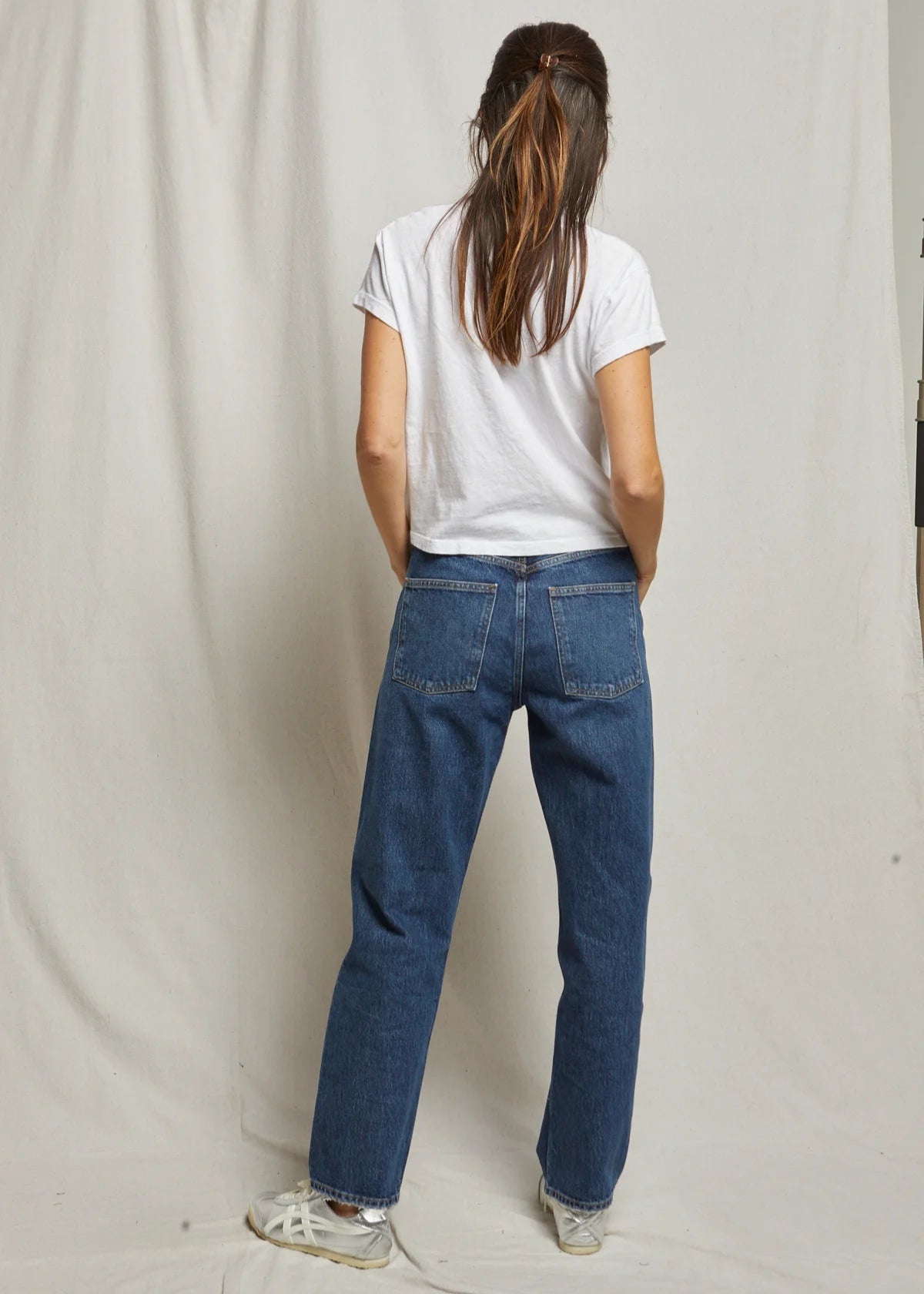 Person wearing a white t-shirt and blue jeans standing against a plain background