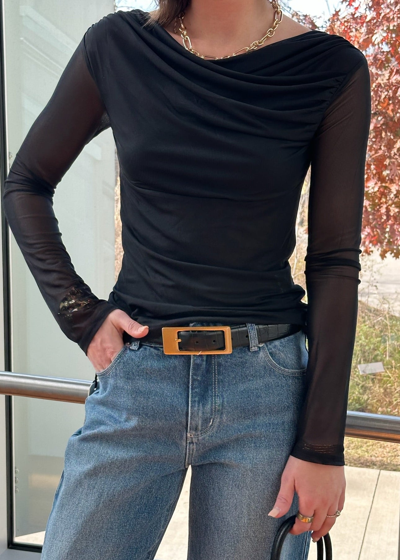 Person wearing a black long-sleeve top with sheer sleeves and blue jeans, standing indoors.