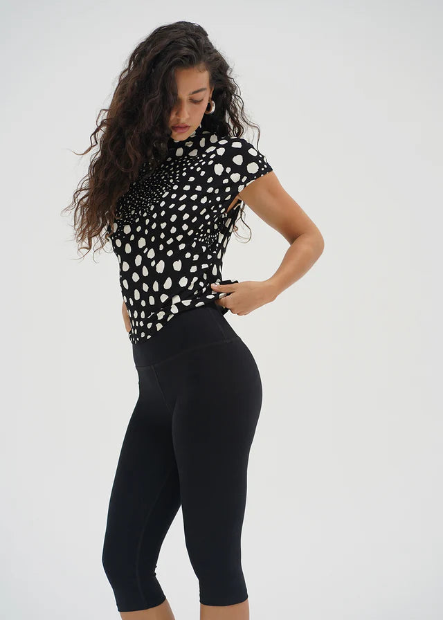 Woman wearing a black and white polka dot top and black leggings on a white background