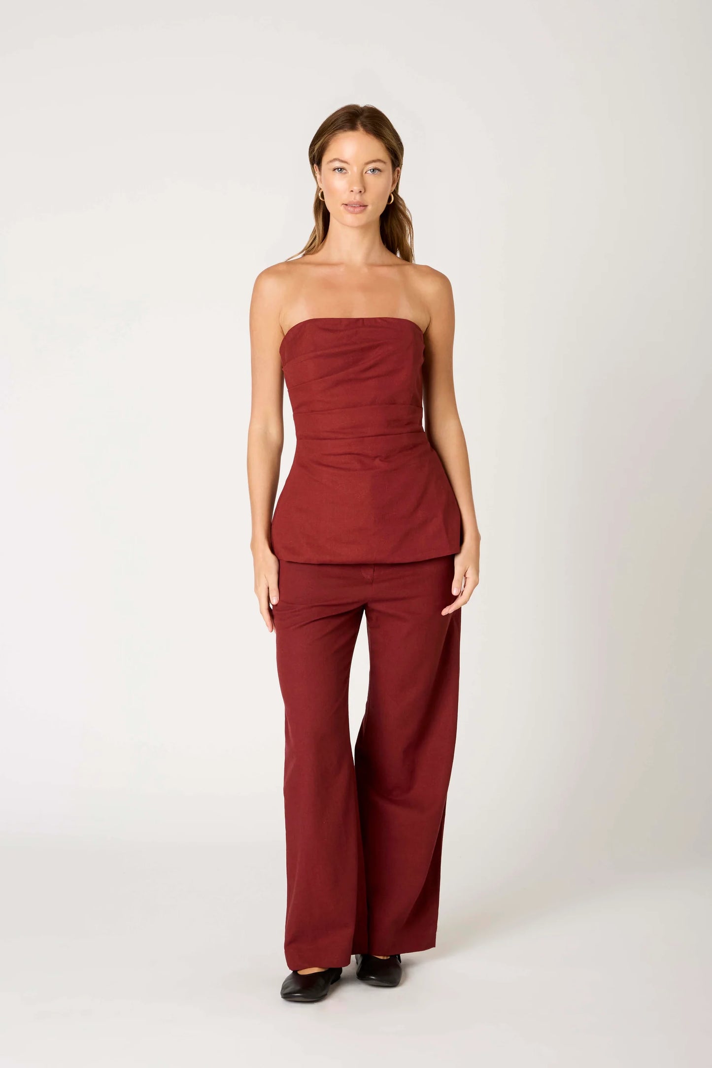 Woman wearing a strapless burgundy jumpsuit on a white background