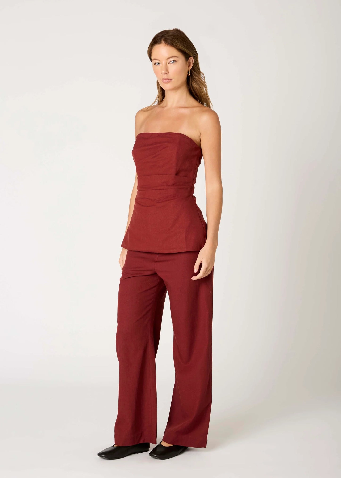 Woman wearing a burgundy strapless top and pants on a white background