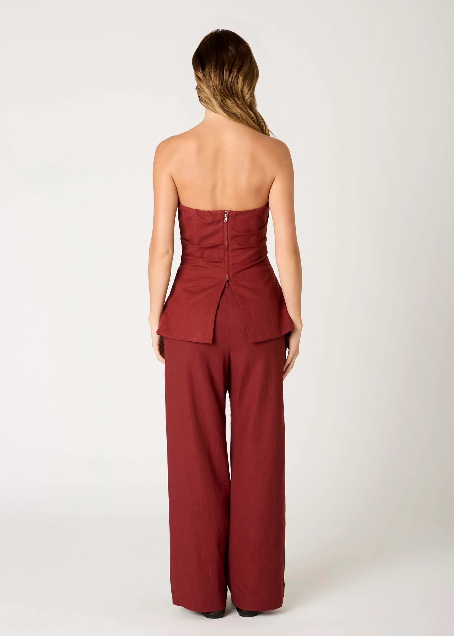 Woman wearing a strapless burgundy jumpsuit on a white background