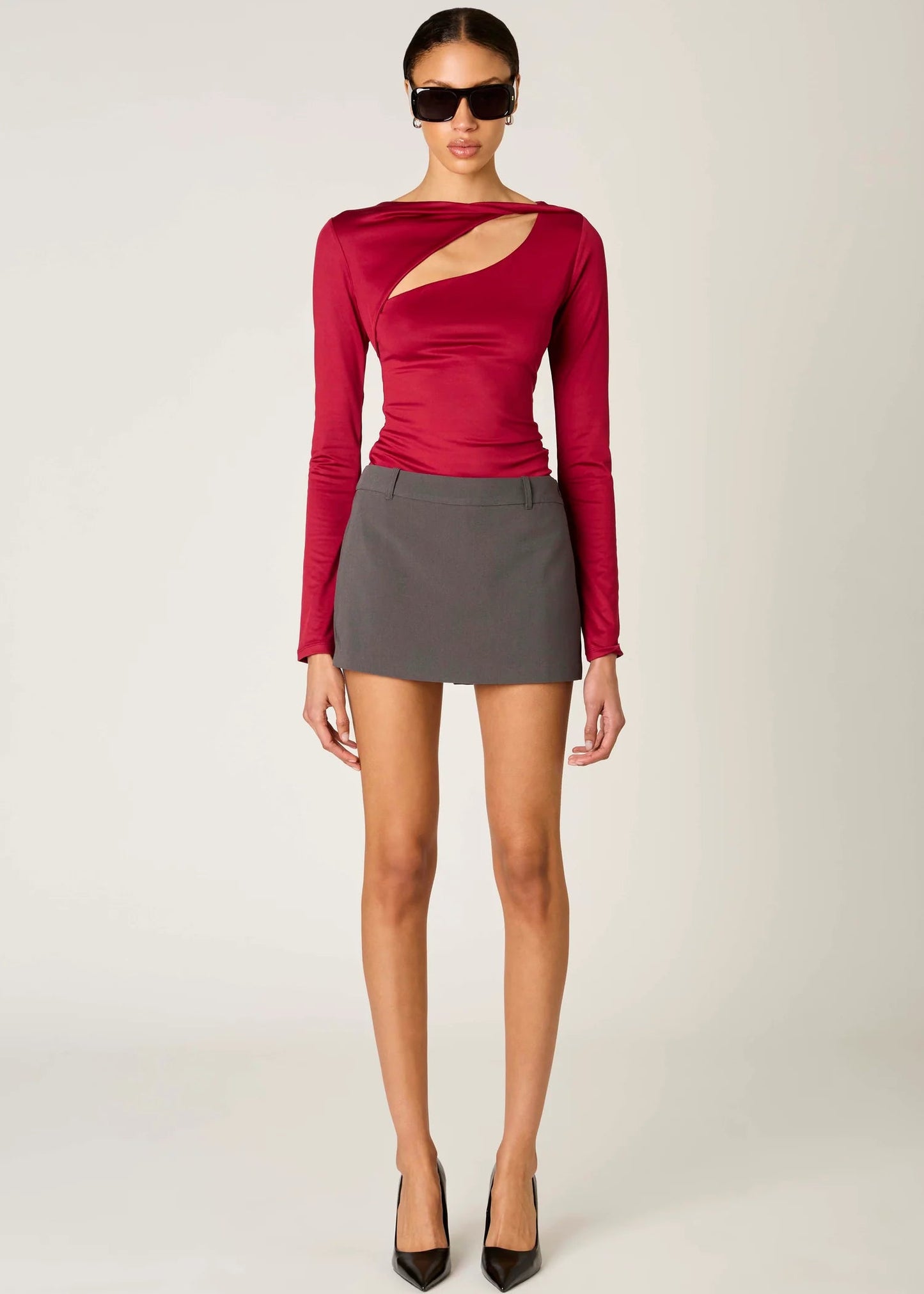 Woman wearing a red long-sleeve top with cut-out design and a gray mini skirt on a white background