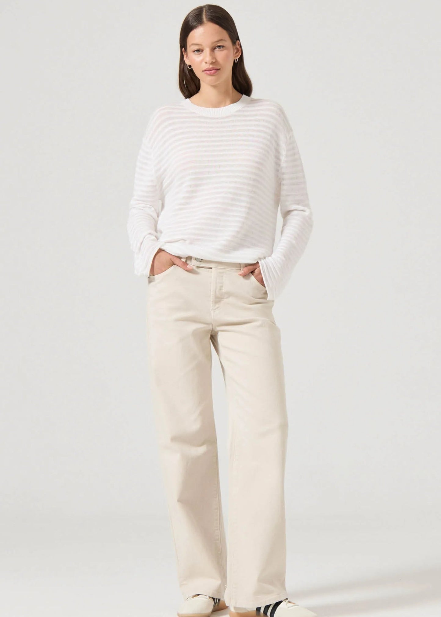 Woman wearing a white striped sweater and beige pants on a plain background