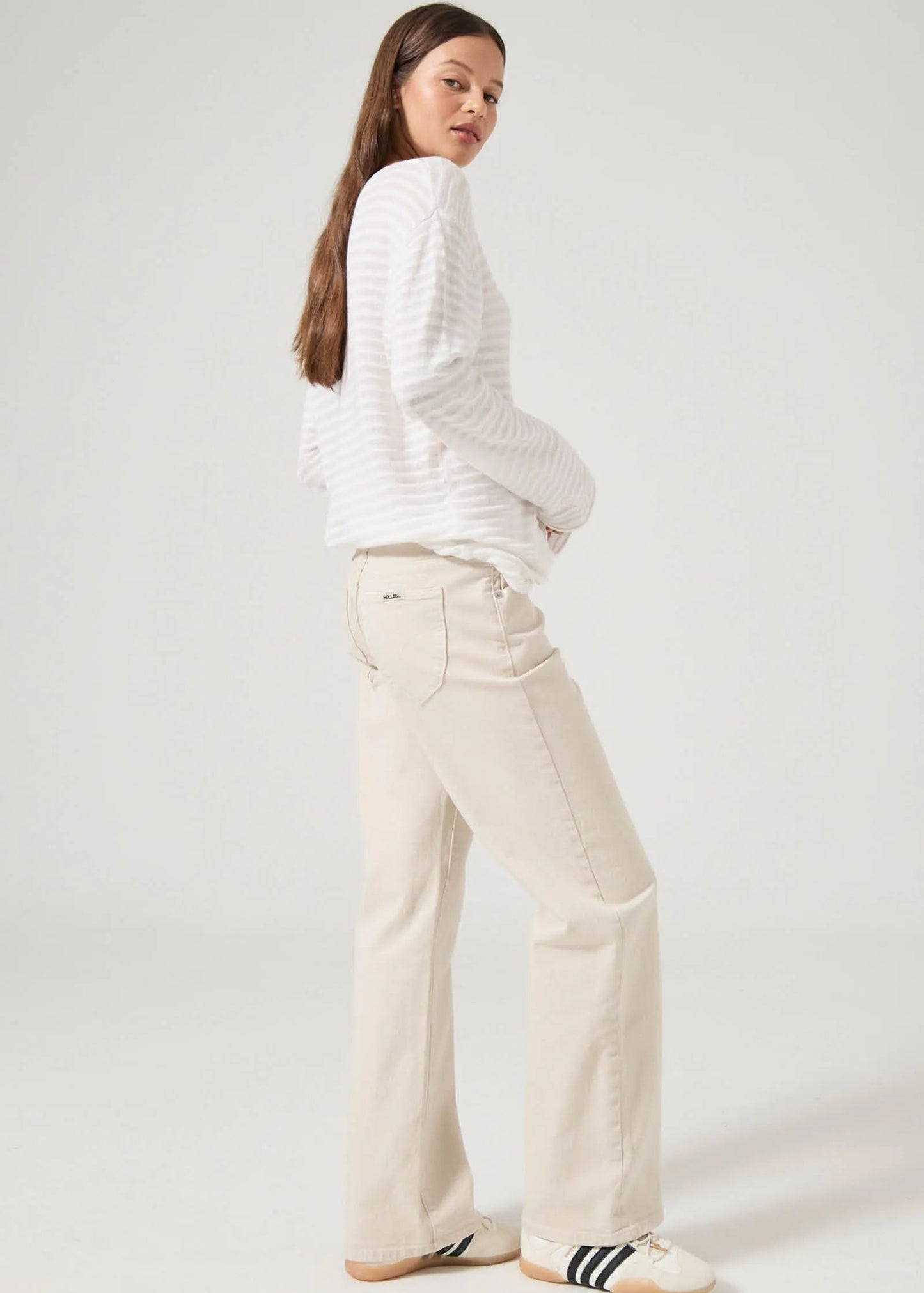 Woman wearing a white sweater and beige pants on a plain background. Rollas denim fayetteville arkansas.