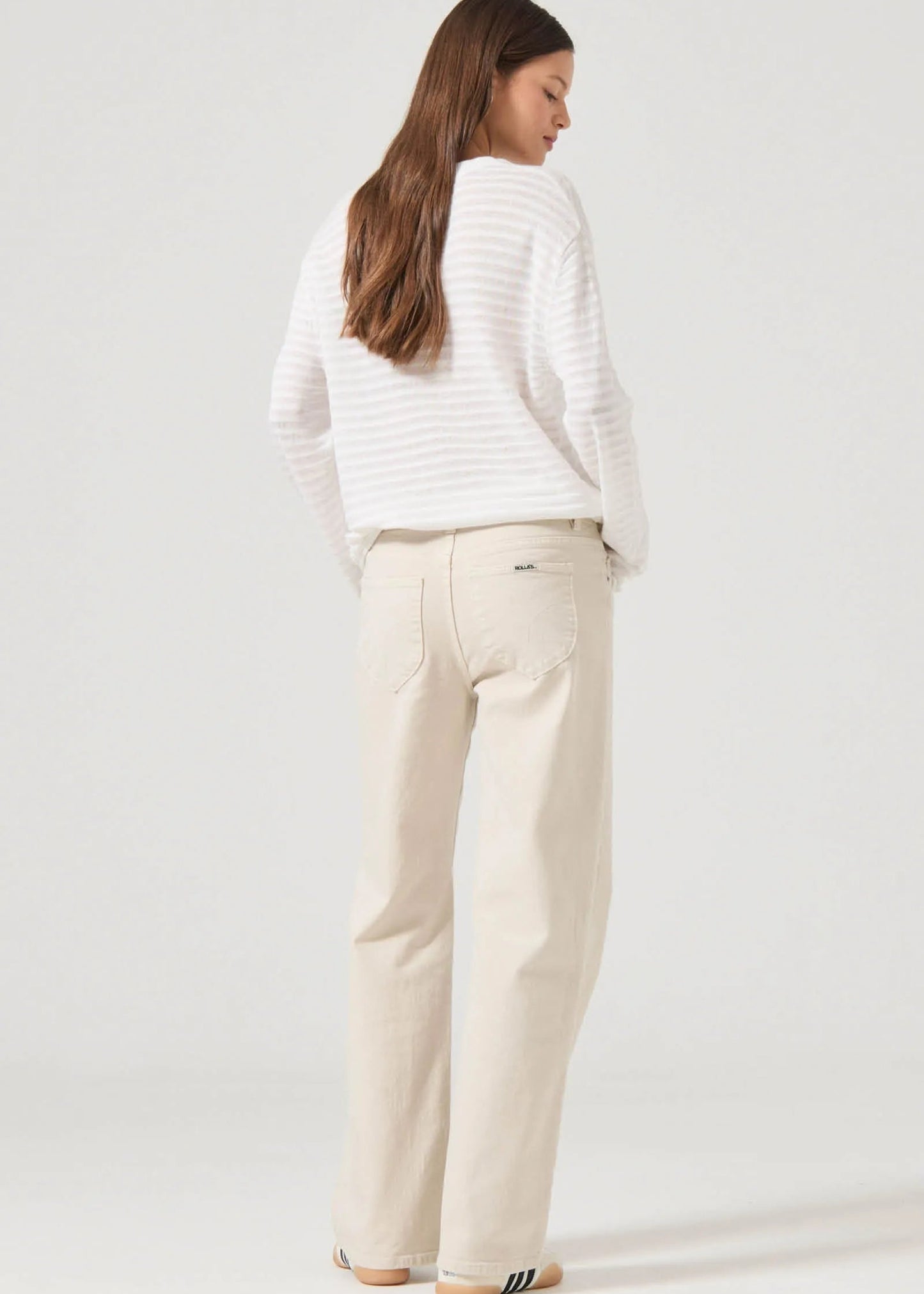 Person wearing a white sweater and beige pants on a plain background. rollas denim. jeans near me. fayetteville arkansas.