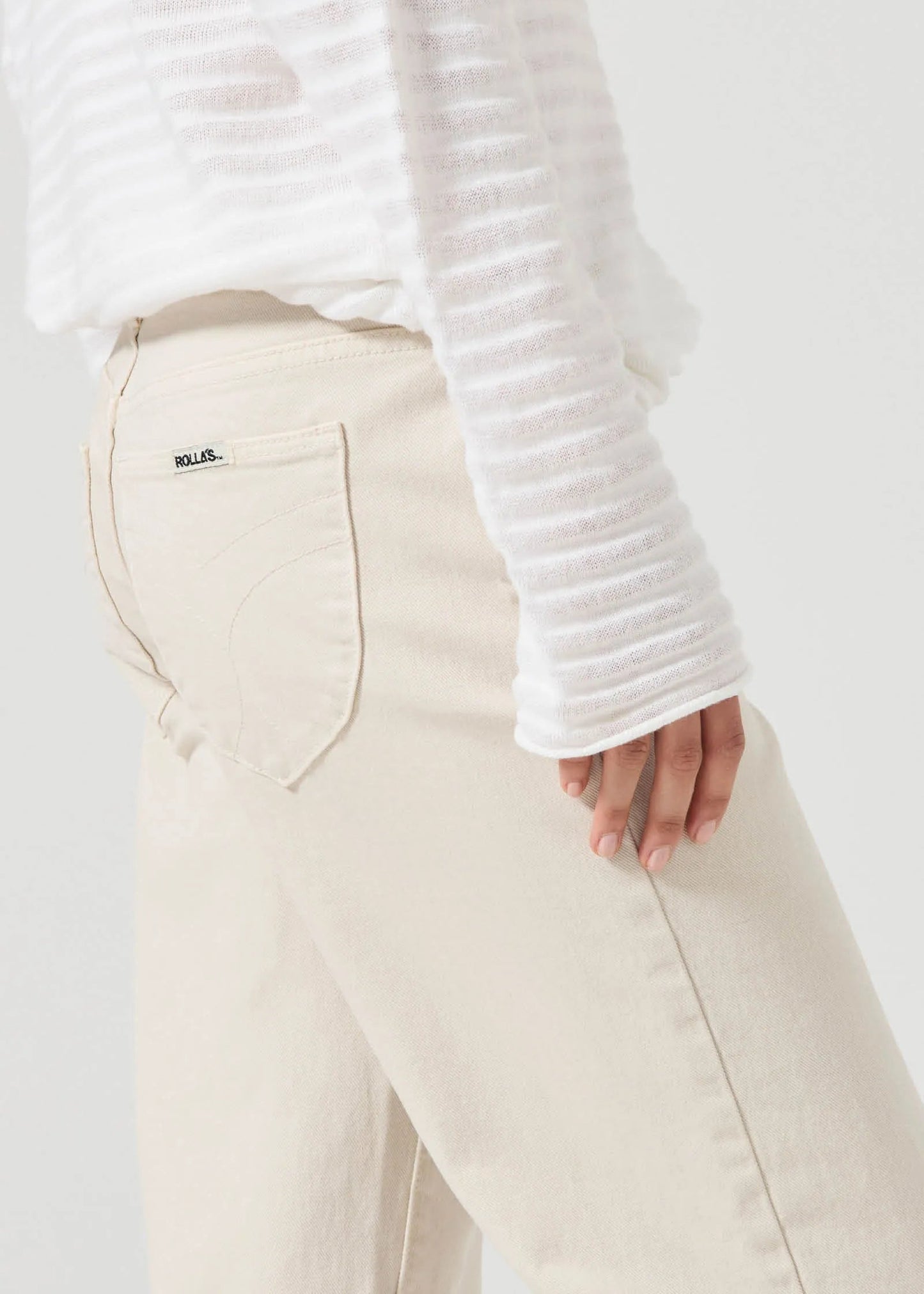 Person wearing a white textured sweater and beige pants on a plain background