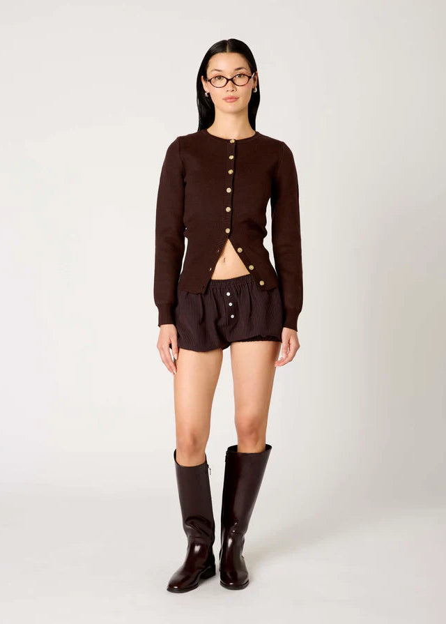 Person wearing a brown cardigan, shorts, and boots on a white background