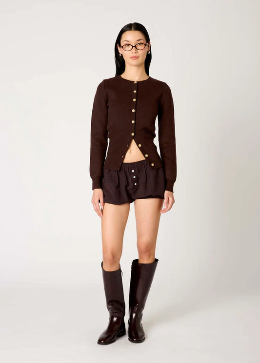 Person wearing a brown cardigan, shorts, and boots on a white background