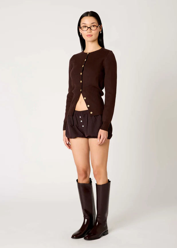 Person wearing a brown cardigan, skirt, and knee-high boots on a white background