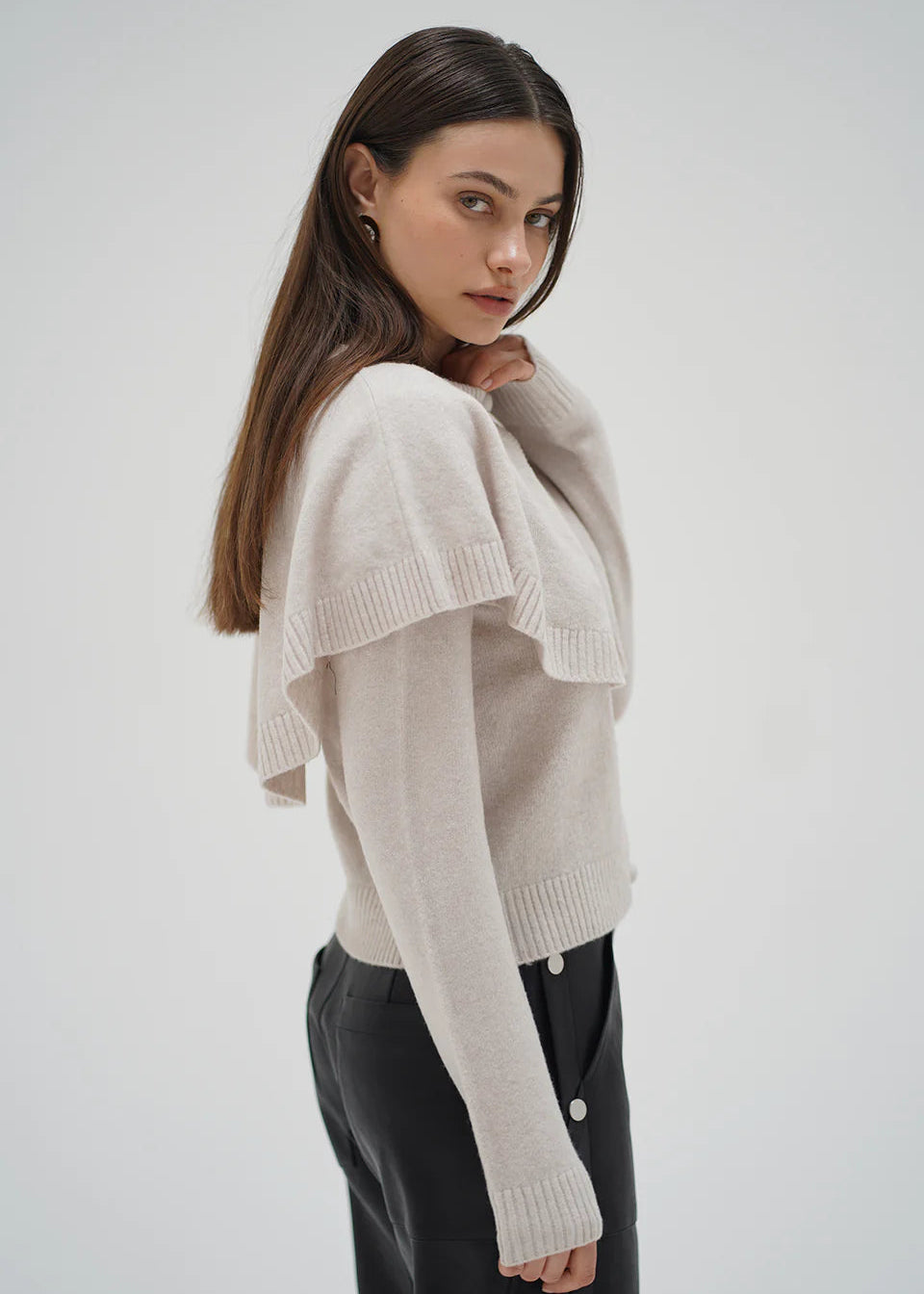 Woman wearing a beige sweater and black pants on a white background