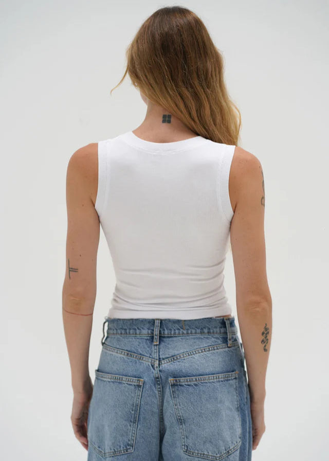 Person wearing a white tank top and blue jeans against a plain background