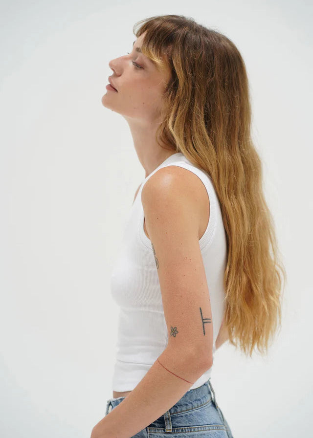 Woman wearing a white tank top and blue jeans against a plain background