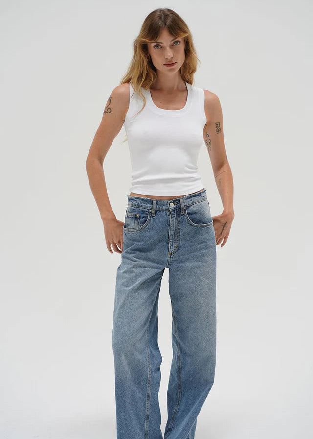 Woman wearing a white tank top and blue jeans on a plain background