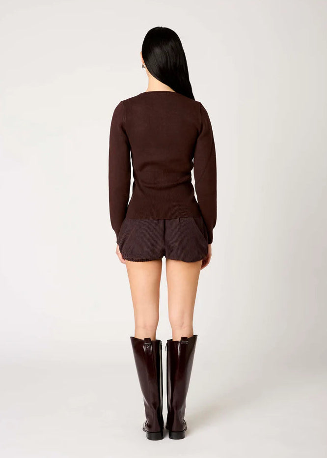 Person wearing a brown sweater and shorts with matching boots on a white background