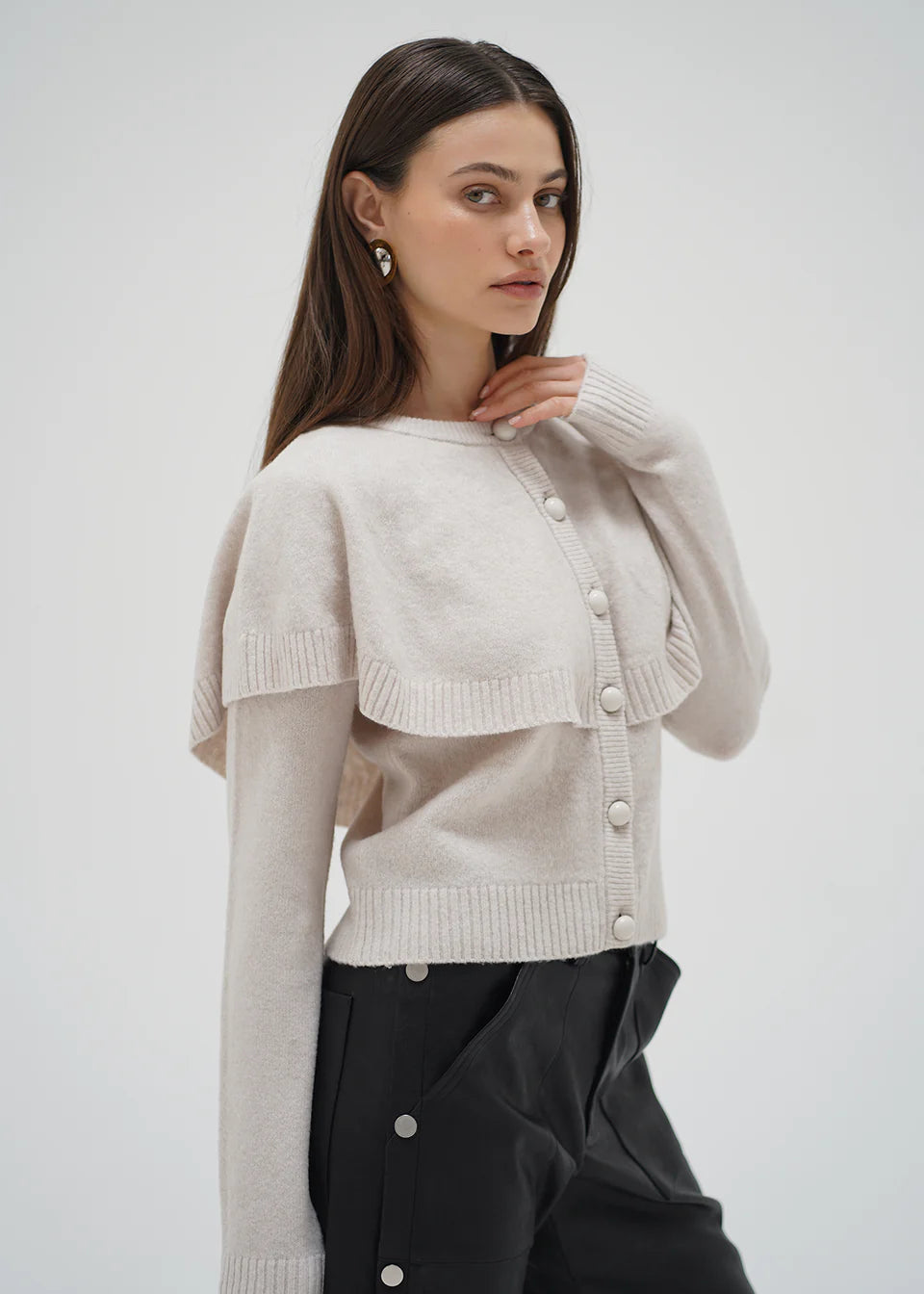 Woman wearing a beige cardigan over a black outfit on a white background