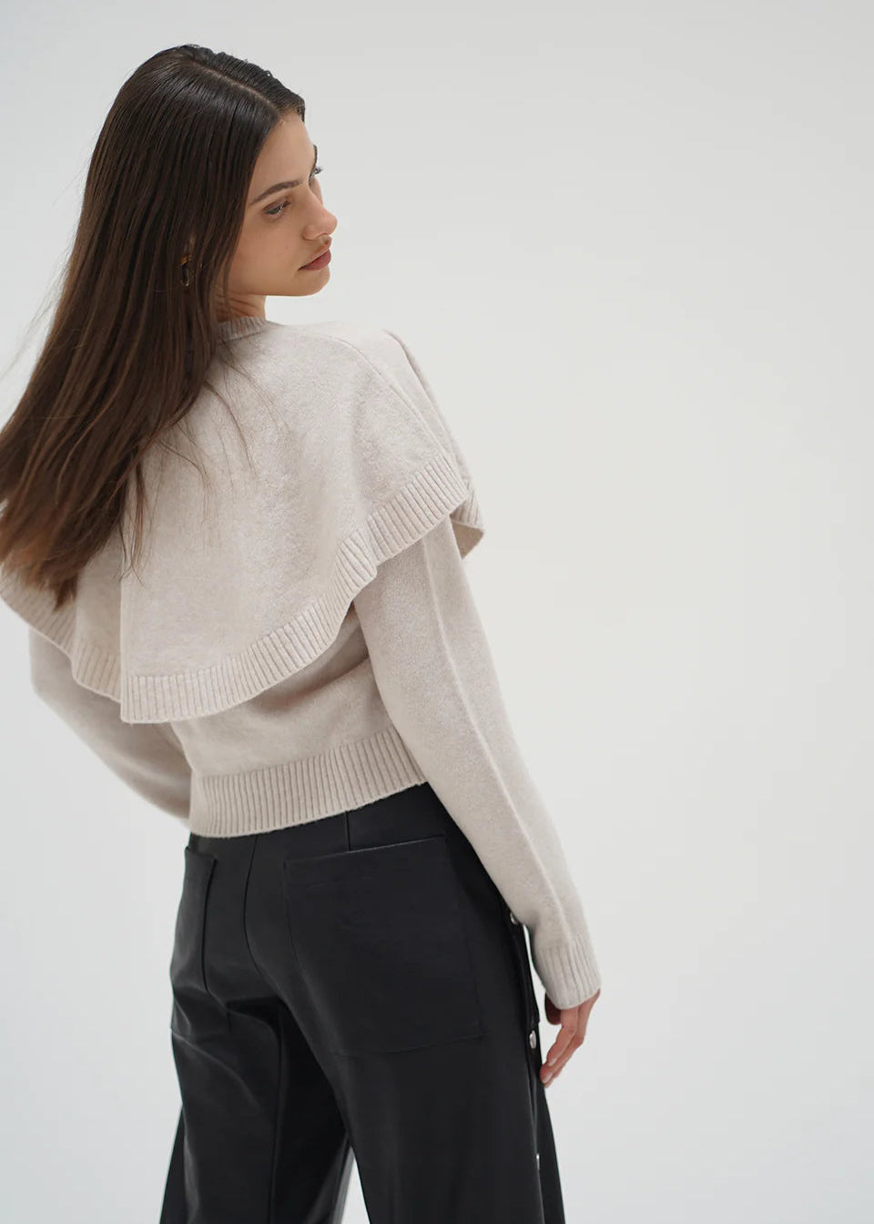 Woman wearing a beige knitted sweater with ruffled shoulders on a white background