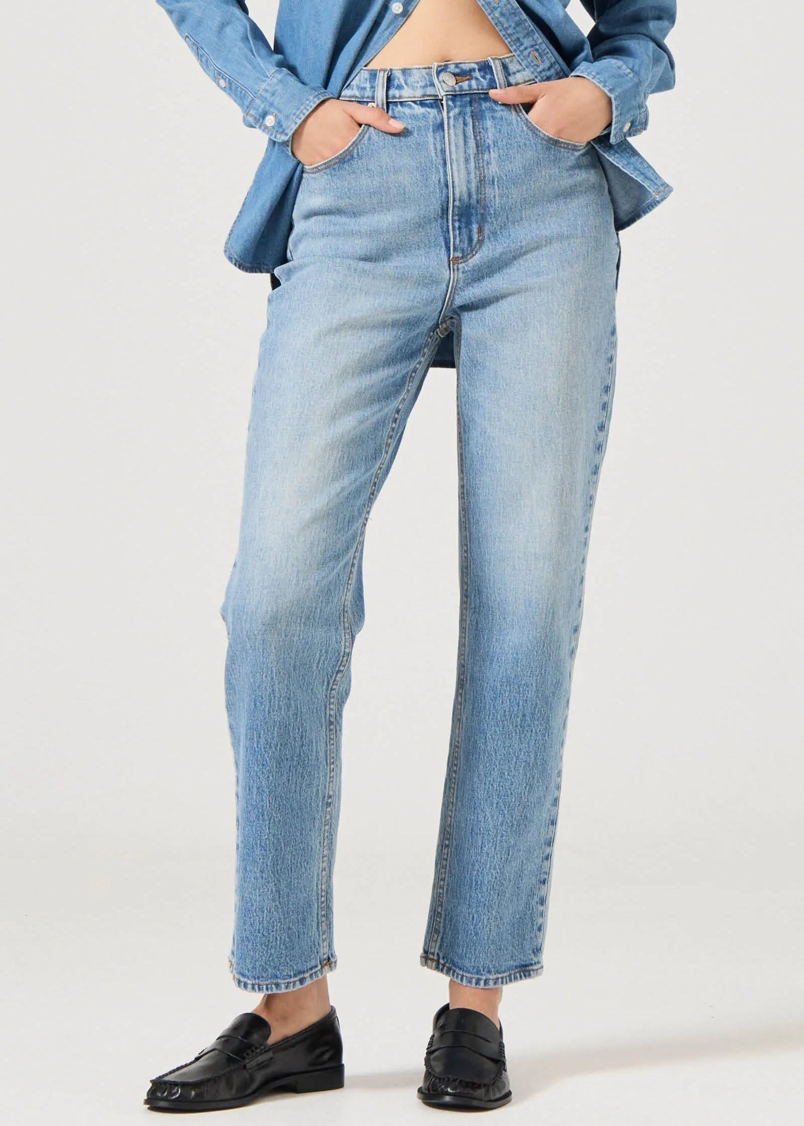 Person wearing light blue jeans and a denim jacket on a white background