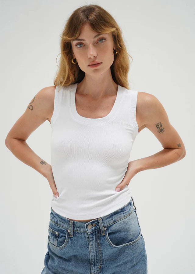 Woman wearing a white tank top and blue jeans against a plain background