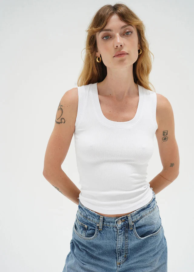 Woman wearing a white tank top and blue jeans against a plain background