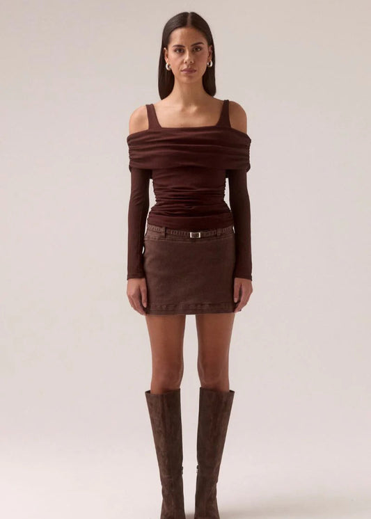 Woman wearing a brown off-shoulder top and skirt with knee-high boots on a white background