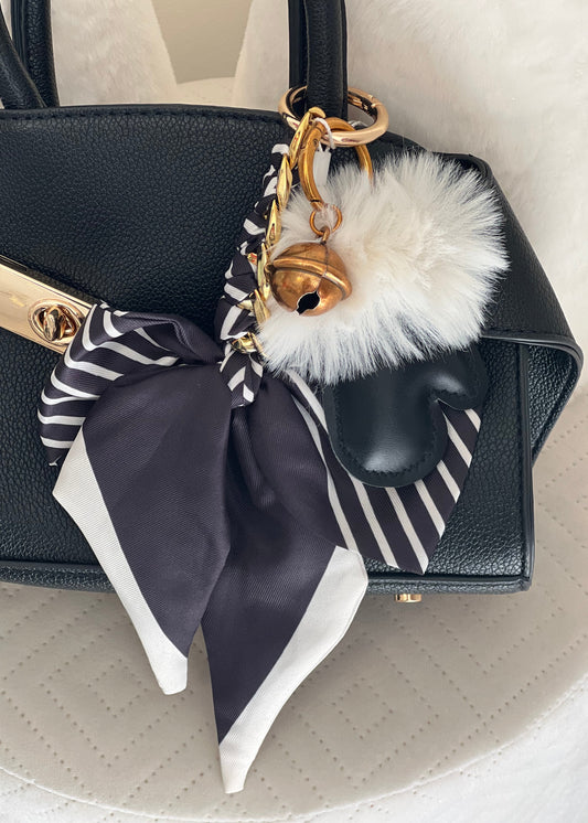 Black handbag with decorative bow and fluffy pom-pom on a light background