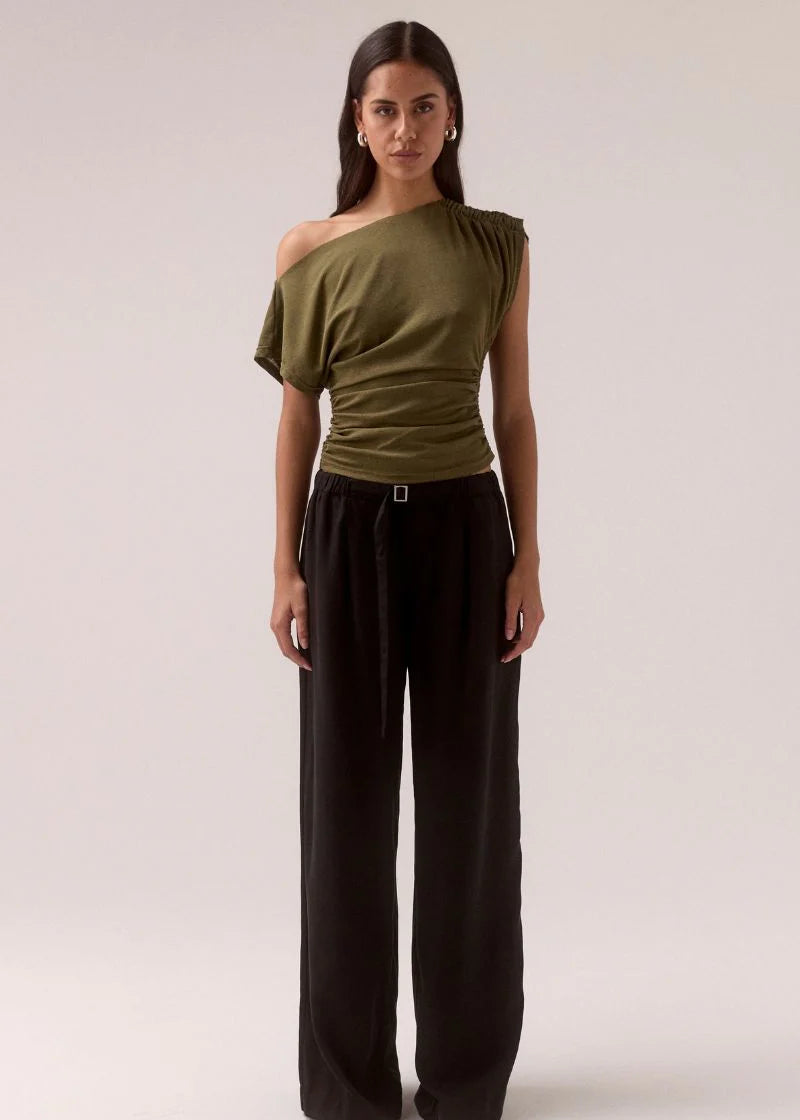 Woman wearing an olive green off-shoulder top and black wide-leg pants on a white background