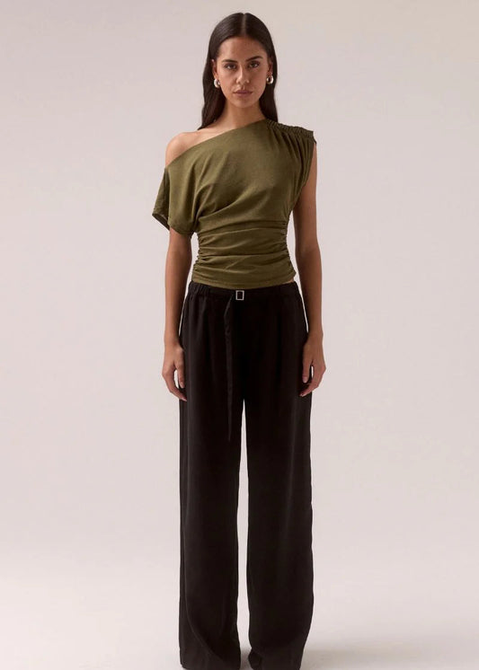 Woman wearing an olive green off-shoulder top and black wide-leg pants on a white background