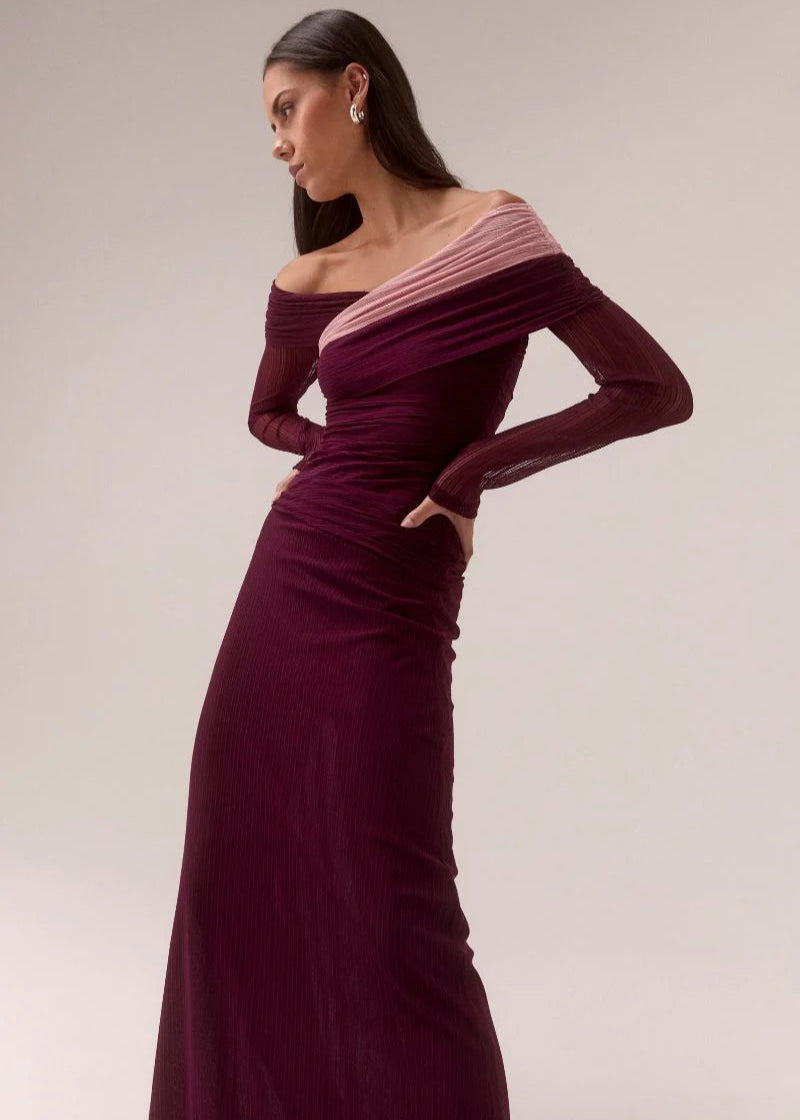 Woman wearing a burgundy off-shoulder gown with long sleeves on a plain background
