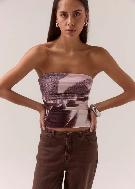 Woman wearing a strapless top with abstract pattern and high-waisted pants on a plain background