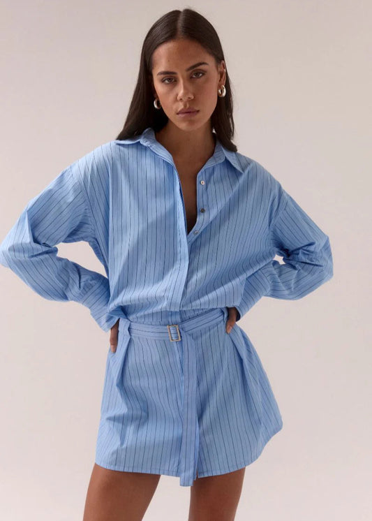 Woman wearing a blue striped shirt and shorts set against a plain background
