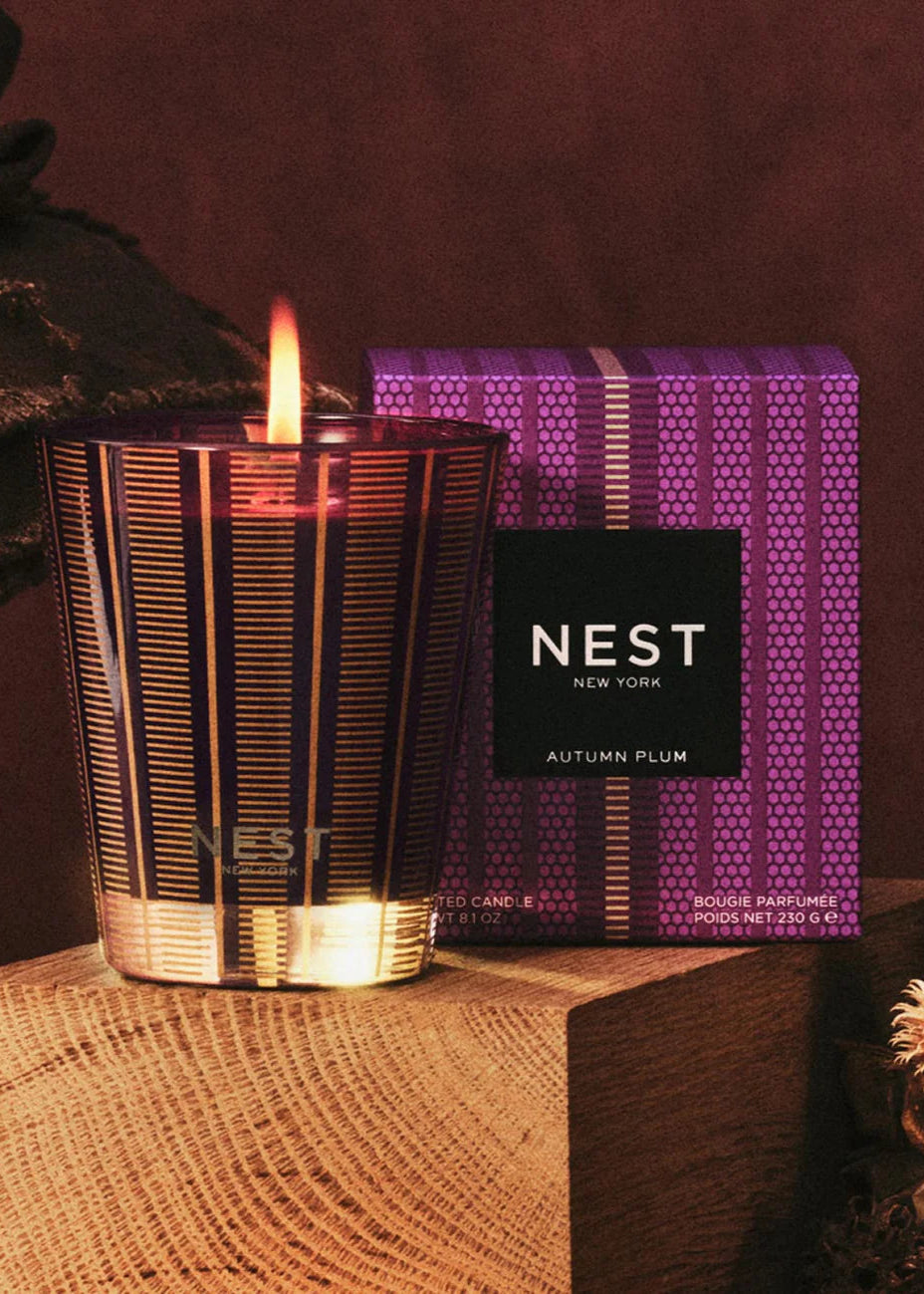 Candle with a lit wick and NEST box on a textured surface