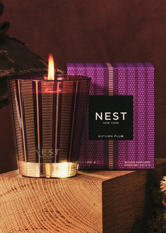 Candle with a lit wick and NEST box on a textured surface