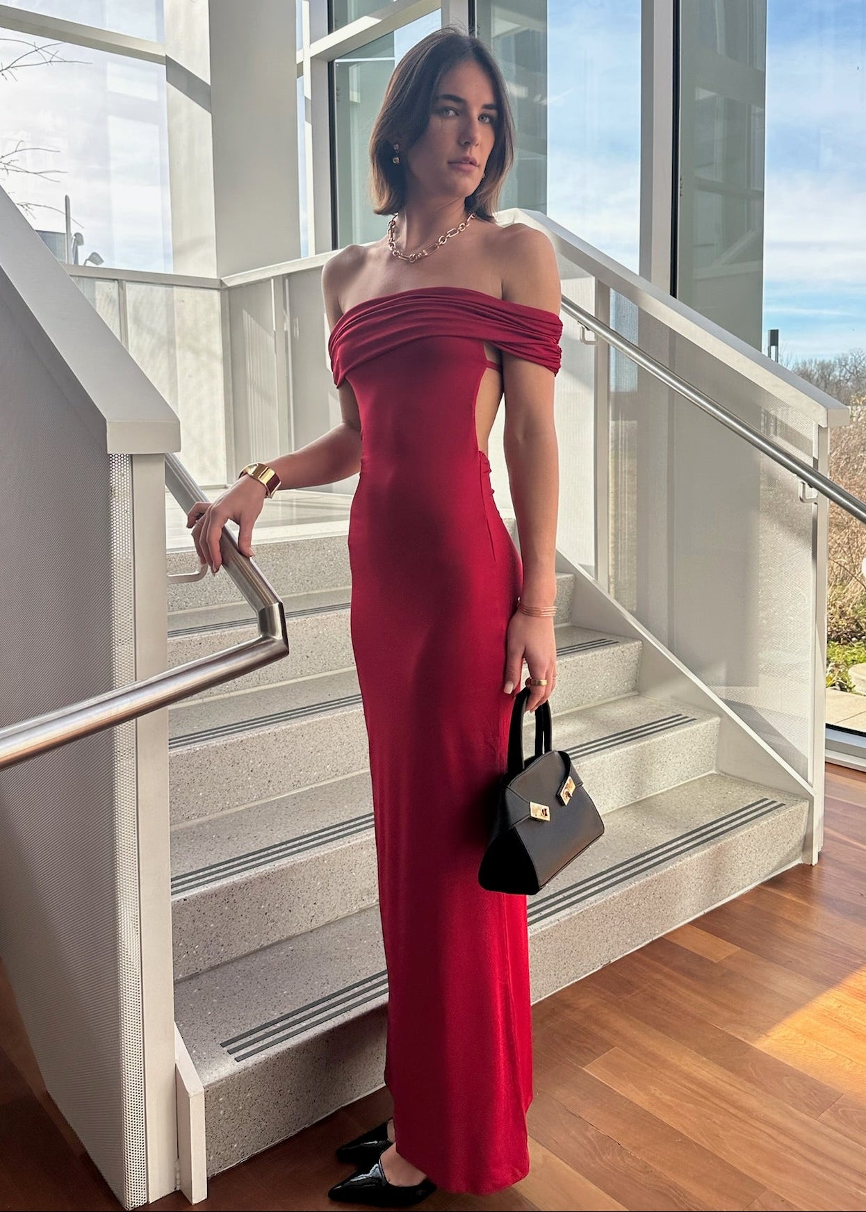 Woman in a red dress standing on a staircase with large windows in the background