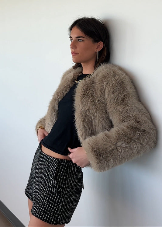 Woman wearing a brown fur jacket against a white wall