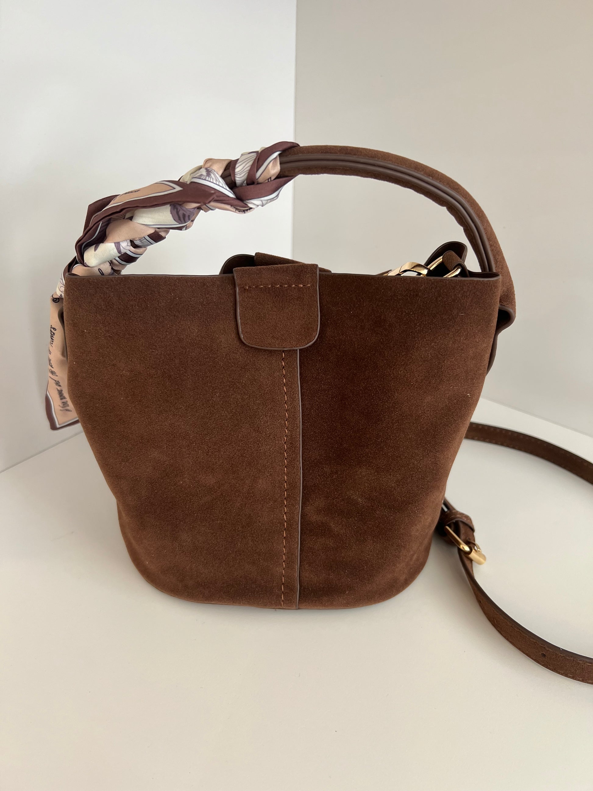 Brown suede handbag with a floral patterned lining on a white surface