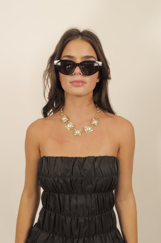 Woman wearing a black strapless dress and sunglasses against a beige background