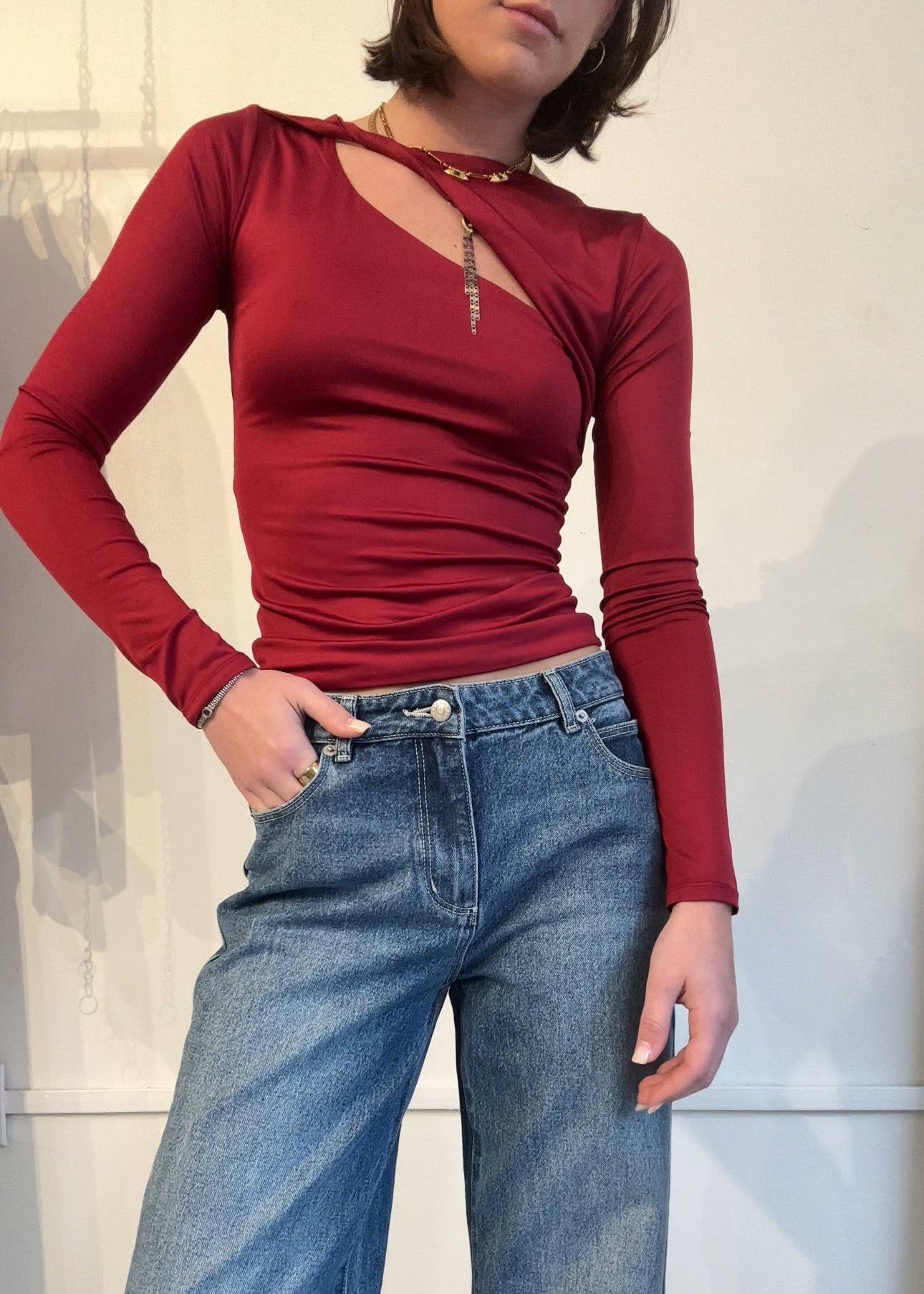 Person wearing a red long-sleeve top and blue jeans against a neutral background