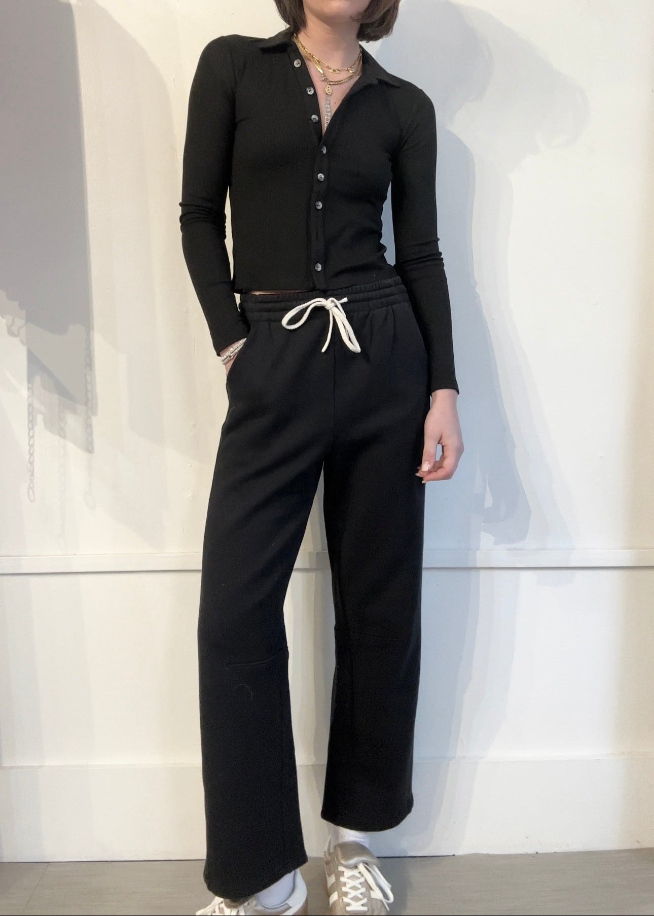 Woman wearing a black outfit with white sneakers in a minimalistic setting