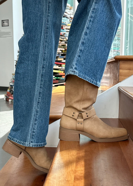 Person wearing tan boots and blue jeans standing on a wooden bench indoors.