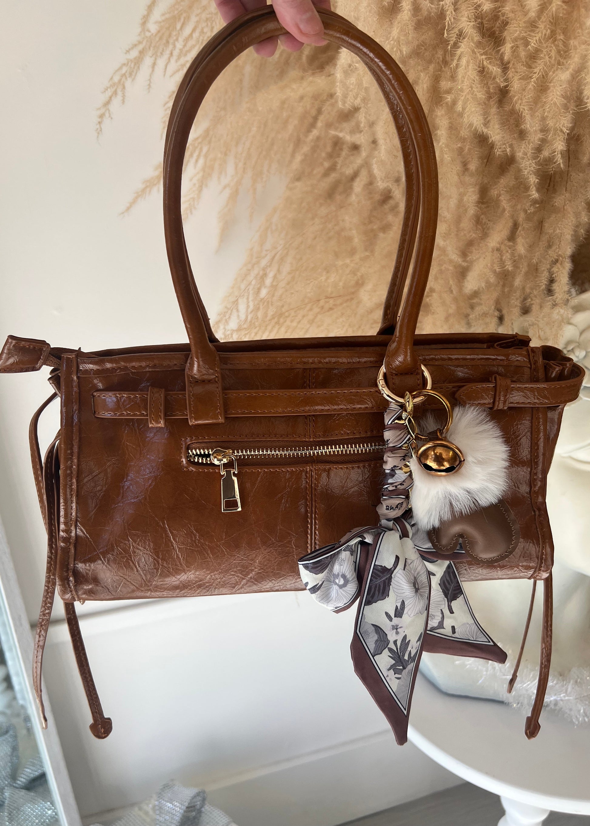 Brown leather handbag with decorative keychain on a marble surface