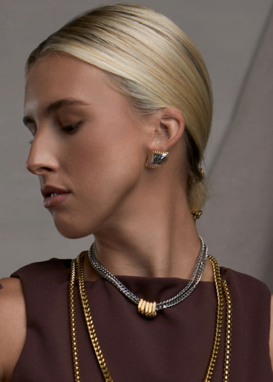 Woman wearing multiple gold necklaces and earrings against a neutral background