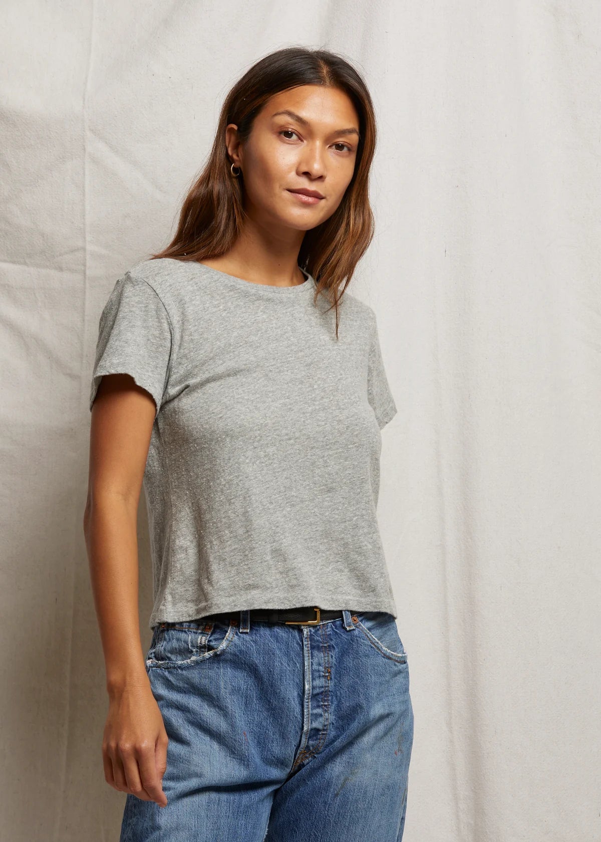Woman wearing a gray t-shirt and blue jeans against a plain background