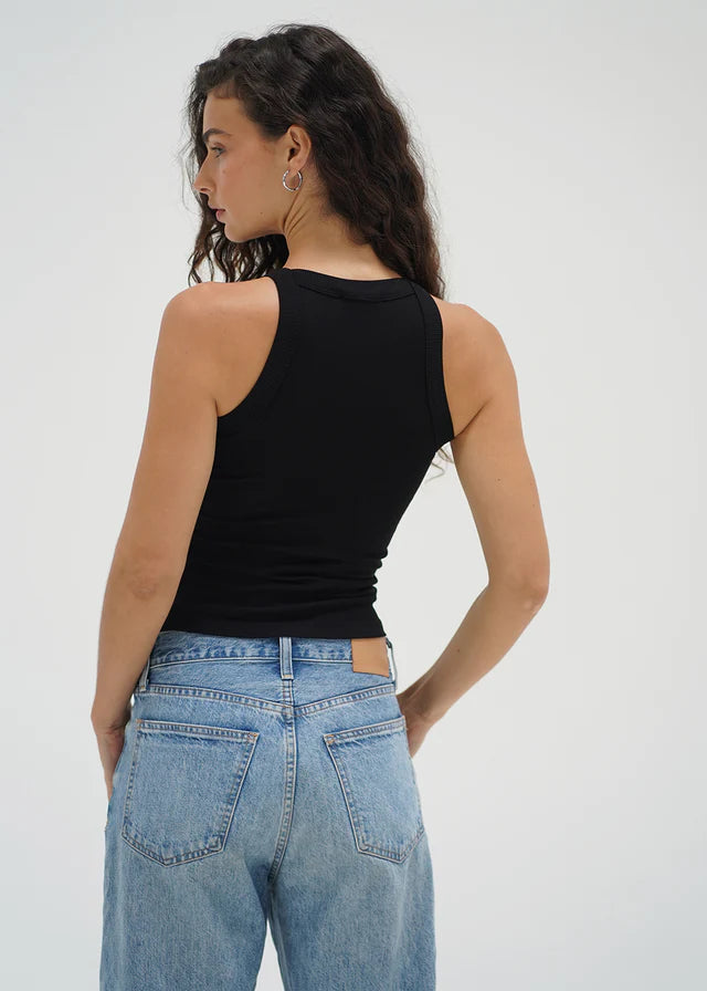 Woman wearing a black tank top and blue jeans against a white background