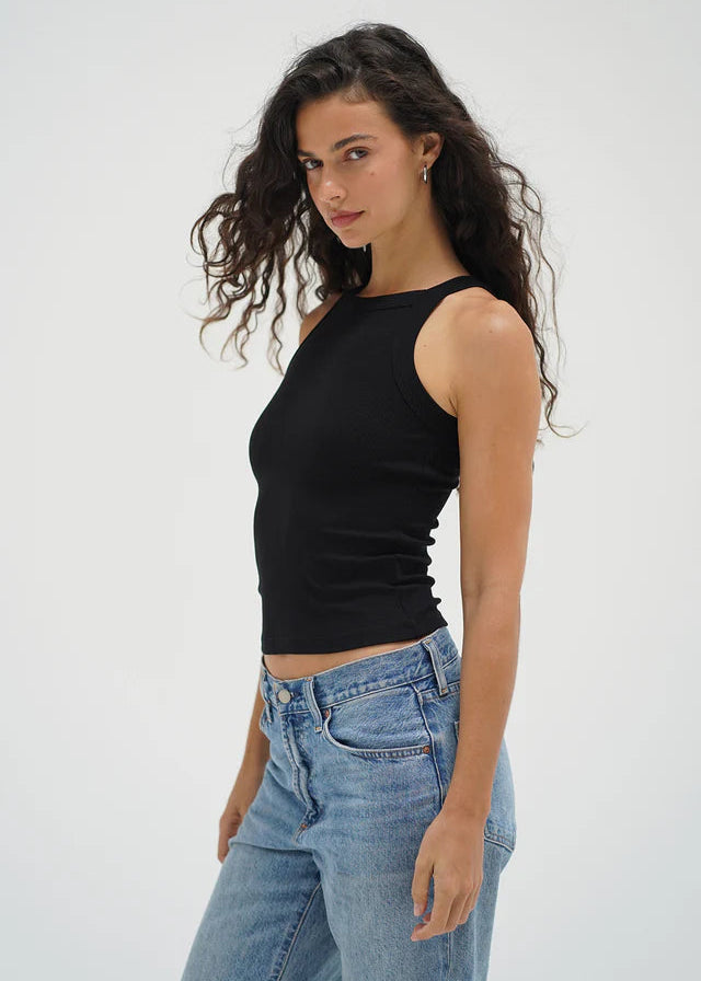 Woman wearing a black sleeveless top and blue jeans against a white background