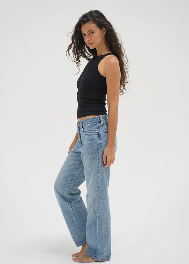 Woman wearing a black sleeveless top and light blue jeans on a white background