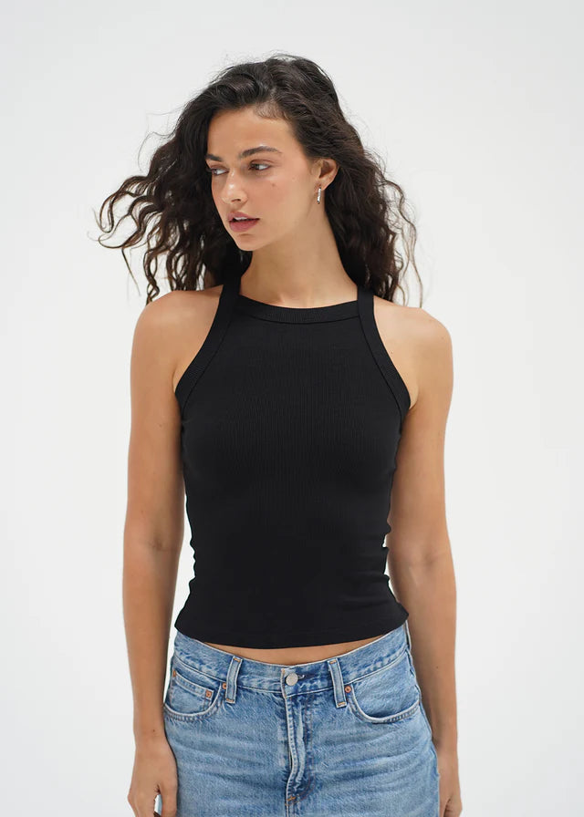 Woman wearing a black tank top and blue jeans against a white background