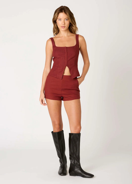 Woman wearing a red romper with cut-out design and black knee-high boots on a white background